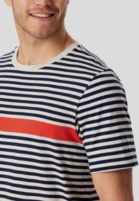 Striped t-shirt featuring horizontal navy and cream stripes, with a bold red horizontal stripe across the chest and a crew neckline.
