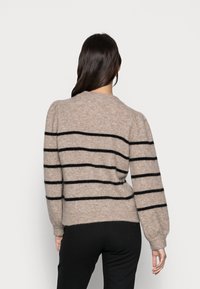 Beige Pullover mit schwarzen horizontalen Streifen, strukturiertem Strickstoff, rundem Ausschnitt und leicht gepufften Ärmeln, kombiniert mit schwarzen Hosen.