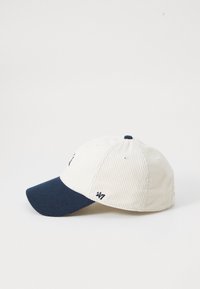 Corduroy cap featuring a cream-colored top and a navy blue visor. Includes small embroidered logo and eyelets for ventilation.