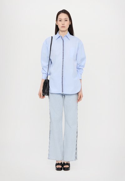 Light blue button-up shirt with a decorative trim, paired with wide-leg light denim jeans featuring side details, and platform black shoes.