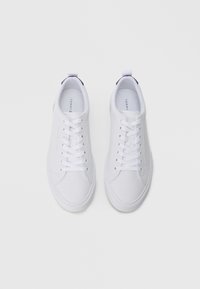 Weiße Sneaker mit glatter Textur, runder Zehenform und Gummisohle. Sie verfügen über flache Schnürsenkel und eine kleine Lasche an der Ferse in einer contrasting Farbe.