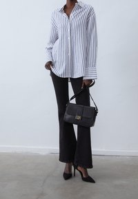 Striped long-sleeve shirt in blue and white, paired with black flared jeans. Black handbag with a textured pattern and gold hardware. Black heels.