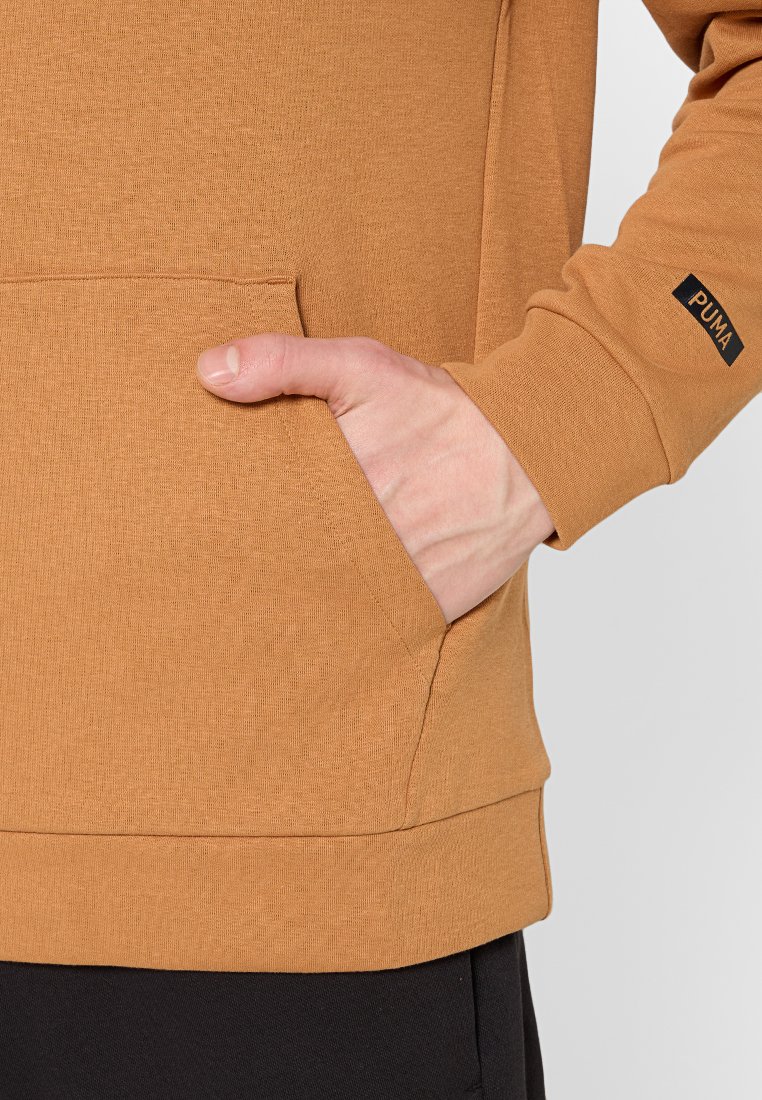 Bruine pullover met een gestructureerde oppervlakte, voorzien van een kengurutas en een klein zwart Puma-logo op de mouw.