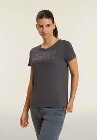 Camiseta gris de manga corta hecha de tela suave, con un diseño embellecido con strass en la parte frontal, combinada con pantalones de chándal grises.