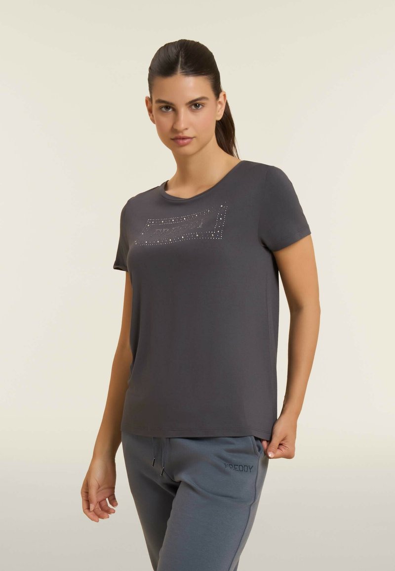 Camiseta gris de manga corta hecha de tela suave, con un diseño embellecido con strass en la parte frontal, combinada con pantalones de chándal grises.