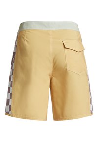 Bañador amarillo con cintura verde, que presenta un patrón de tablero de ajedrez en marrón y blanco en los laterales y un detalle de bolsillo en la parte posterior.