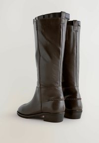 Stivali alti in pelle marrone con una texture liscia, tacco basso e cuciture rinforzate, che mostrano un design classico e una costruzione robusta.