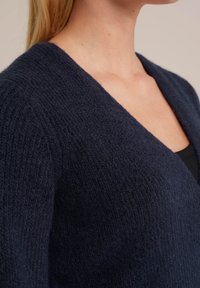 Temno modri pleteni kardigan z globokim V-izrezom, ki se ponaša z teksturirano, mehko tkanino in ohlapnim krojem. Primeren za plastenje čez majice.