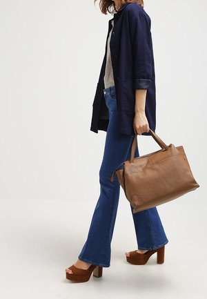 Ruskea nahkalaukku, jossa on sileä pinta ja kaksi kahvaa, yhdistettynä tummansiniiseen bleiseriin, raidalliseen toppiin ja leveälahkeisiin farkkuihin. Ruskeat korkokengät.