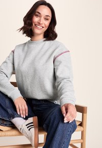 Light gray sweatshirt with red stitching on shoulders, ribbed cuffs, and crew neckline, paired with blue jeans and light sneakers.