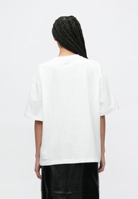 Biała bawełniana koszulka o luźnym kroju, z krótkimi rękawami i okrągłym dekoltem, z subtelnym logo na górnej części pleców.