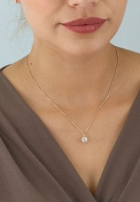 Gold chain necklace featuring a clear, oval-cut stone pendant, set against a textured brown top.