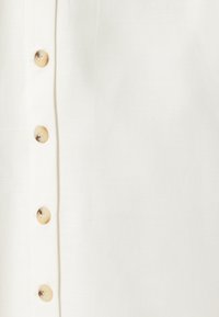 Chemise blanche à boutons, en tissu texturé, avec six boutons ronds de couleur claire sur le devant et sans motifs ni accents visibles.