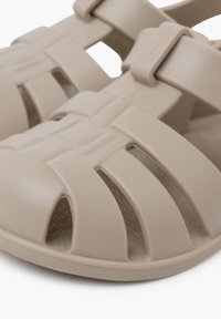 Beez plastmassist sandaalid, millel on ristkülikukujuline disain ja avatud varvas. Sile tekstuur, millel on ümmargune muster sisetallal.