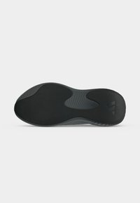 Semelle noire de chaussure de sport avec motifs de grip texturés et logo Adidas près du talon, montrée sur un fond clair uni.