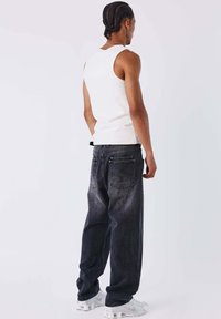 Camiseta de tirantes blanca combinada con vaqueros de corte holgado en gris oscuro, con bolsillos traseros y un sutil degradado. La modelo lleva zapatillas blancas.