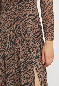 Kleid mit braunem und schwarzem Tierdruck, das lange Ärmel, einen Seitenschlitz und Falten-Details für zusätzliche Textur bietet.