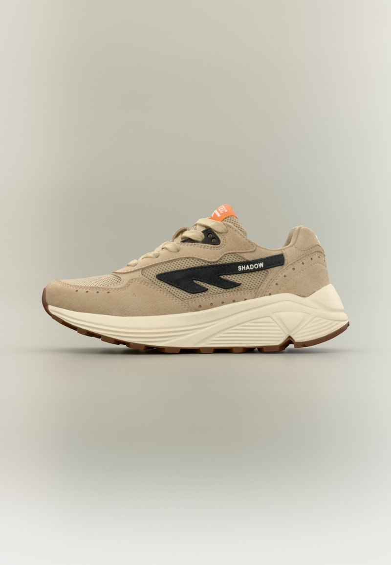 Μπεζ αθλητικό παπούτσι με επάνω μέρος από δίχτυ και σουέτ, μαύρες πλαϊνές λεπτομέρειες, λευκή μεσαία σόλα, πορτοκαλί ετικέτα και υφή εξωτερικής σόλας από καουτσούκ.