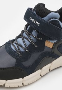 Granatowe i jasnoniebieskie buty sportowe wykonane z zamszu i siateczki, z czarnymi sznurowadłami, rzepem oraz teksturowaną gumową podeszwą.