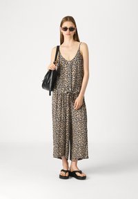 Jumpsuit s uzorkom leoparda, s opuštenim krojem, tanjim naramenicama i strukiranim strukom, uparen s crnim sandalama i strukturiranom crnom torbom.