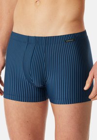 Navy blue boxer shorts feature vertical stripes in varying shades, smooth texture, elastic waistband, and a logo label at the waist.