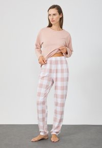 Lyserød langærmet top med afslappet pasform, parret med hvide og lyserøde ternede pyjamasbukser med elastisk talje og manchetter.