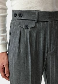 Grijze streepjesbroek van textuurstof, met dubbele knopen en plooien in de taille voor een gestructureerd silhouet.