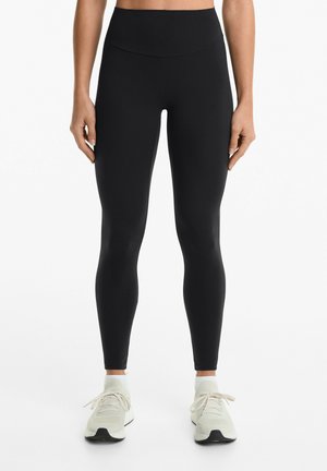 Leggings neri con vita alta, realizzati in tessuto elasticizzato. Tessuto morbido, design aderente e abbinati a scarpe da ginnastica chiare.