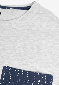 Grå bomulds t-shirt med rund hals og en navy lomme med hvidprikket mønster. Blødt, tekstureret stof med kontrasterende detaljer.