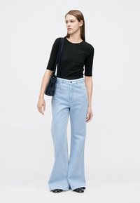 Μαύρο εφαρμοστό μπλουζάκι, ανοιχτό μπλε τζιν με καμπάνα και ψηλή μέση, και μικρό μαύρο τσαντάκι, σε συνδυασμό με μαύρα παπούτσια. Απλός σχεδιασμός και υφή.