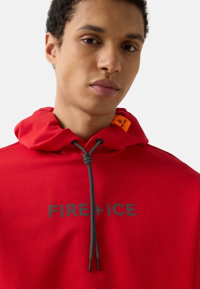 Jeune personne portant un sweat à capuche rouge avec des cordons noirs et l'inscription "FIRE+ICE" sur le devant, regardant droit devant.