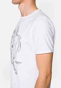 Biała bawełniana koszulka z czarnym rysunkiem konturowym konia, z okrągłym dekoltem i krótkimi rękawami. Widoczne logo marki.