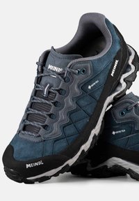 Męskie buty trekkingowe w ciemnoniebieskim zamszu z teksturowanymi panelami, z logo GORE-TEX, szarymi sznurówkami i czarną gumową podeszwą, zaprojektowane do użytku na świeżym powietrzu.