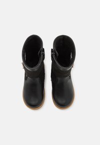 Para czarnych skórzanych i zamszowych botków zimowych z bocznymi zamkami i brązowymi gumowymi podeszwami, pokazanych z góry na białym tle.