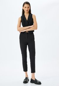 Zwarte op maat gemaakte vest met een lage V-hals, gecombineerd met slim-fit zwarte broek en robuuste zwarte loafers, met een gladde textuur en gestructureerd design.