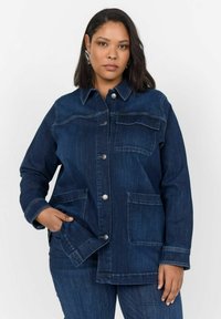 Temno modra denim jakna s sprednjimi snap gumbi, dvema nakladnima žepoma, kontrastnim šivanjem in dolgimi rokavi. Teksturiran, sproščen dizajn.