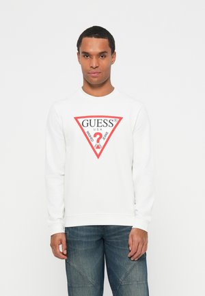 Bijela dukserica s okruglim izrezom, s crvenim trokutastim logotipom na kojem piše "GUESS" i znakom pitanja u središtu. Ojačana rebrastim manžetama.
