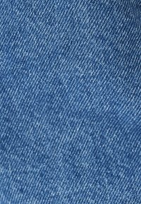 Tessuto denim di un blu chiaro, caratterizzato da una texture morbida con una leggera trama diagonale a spina di pesce. La superficie mostra sottili variazioni di colore.