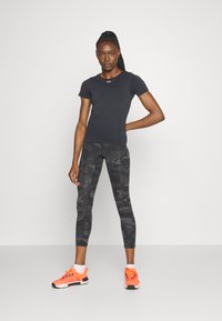 Tricou sportiv negru cu mânecă scurtă, asortat cu colanți gri camuflați, purtat cu adidași portocalii strălucitori. Material neted și croială ajustată.