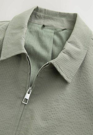 Hellgrüne Zip-Jacke aus strukturiertem Stoff, mit Kragen und einem glatten Reißverschluss mit silbernem Zugband.