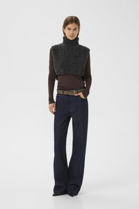 Pull en laine gris foncé avec col roulé, porté par-dessus un haut ajusté à manches longues marron, associé à un jean en denim bleu à jambes larges et une ceinture beige.