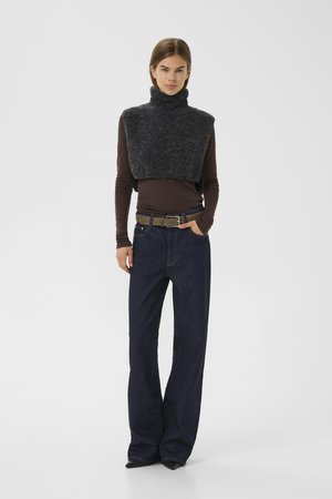 Pullover a collo alto in lana grigia scura abbinato a una maglia marrone a maniche lunghe, indossato con jeans denim blu a gamba larga e una cintura beige.
