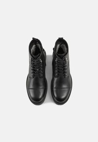 Bottines en cuir noir à finition lisse, avec lacets à l'avant, fermetures éclair latérales et doublure en fourrure douce. Bout arrondi et semelle robuste.