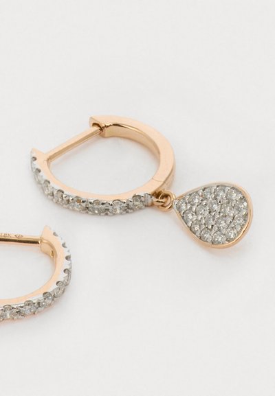 Zeltainā tonī auskari ar teksturētu virsmu, kas aprīkoti ar karājošu piekari, kas ir izrotāts ar caurspīdīgiem kristāliem asaras formā.