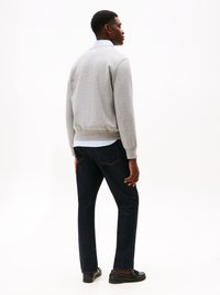 Gray sweatshirt in cotton blend, ribbed cuffs and hem, layered over a light blue collared shirt. Dark denim jeans and black loafers complete the look.