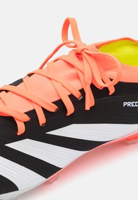 Scarpe da calcio bianco e nero con lacci arancioni brillanti e interno verde lime. Dotate di una tomaia texturizzata e suola con tacchetti stampati.
