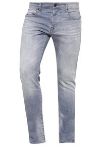 Jeans de mezclilla azul claro con corte ajustado, diseño clásico de cinco bolsillos, un ligero desvanecimiento y cierre de botón en la cintura.