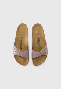 Svetlofialové sandále Birkenstock so širokým popruhom a zlatou sponou, s hnedou koreňovou stielkou a potlačeným logom značky na vnútorných stielkach.