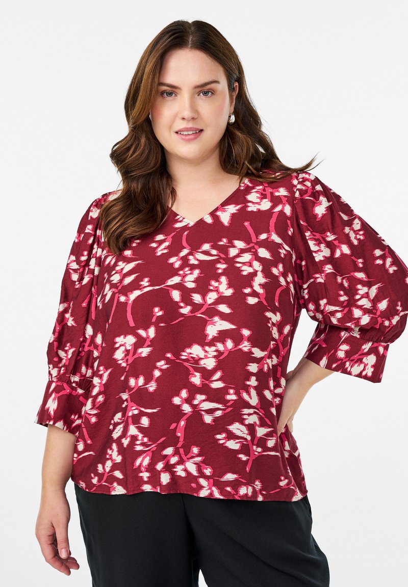 Burgundy-paita, jossa on vaaleanpunaisia ja valkoisia kukkakuosia. Ominaisuuksiin kuuluu V-kaula-aukko ja puffit sekä hihansuiden yksityiskohdat. Pehmeä kangaslaatu.