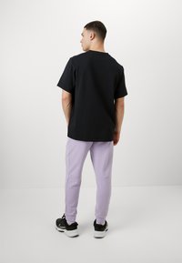 Black short-sleeve t-shirt with a round neckline, paired with light purple sweatpants. The outfit is completed with black athletic shoes.